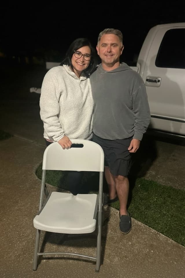 Deke and Samantha standing behind a folding chair, the Pull Up A Chair posture